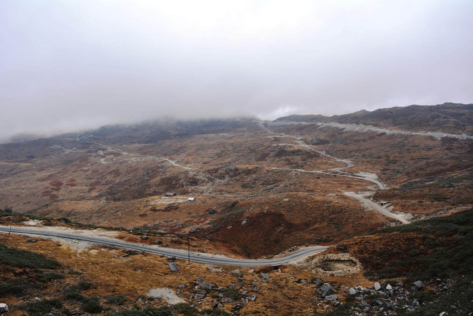 A winding mountain road cutting through barren hills under low cloud