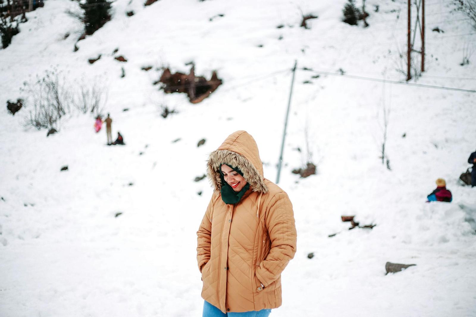 A woman in a hooded winter coat smiling on a snowy hillside