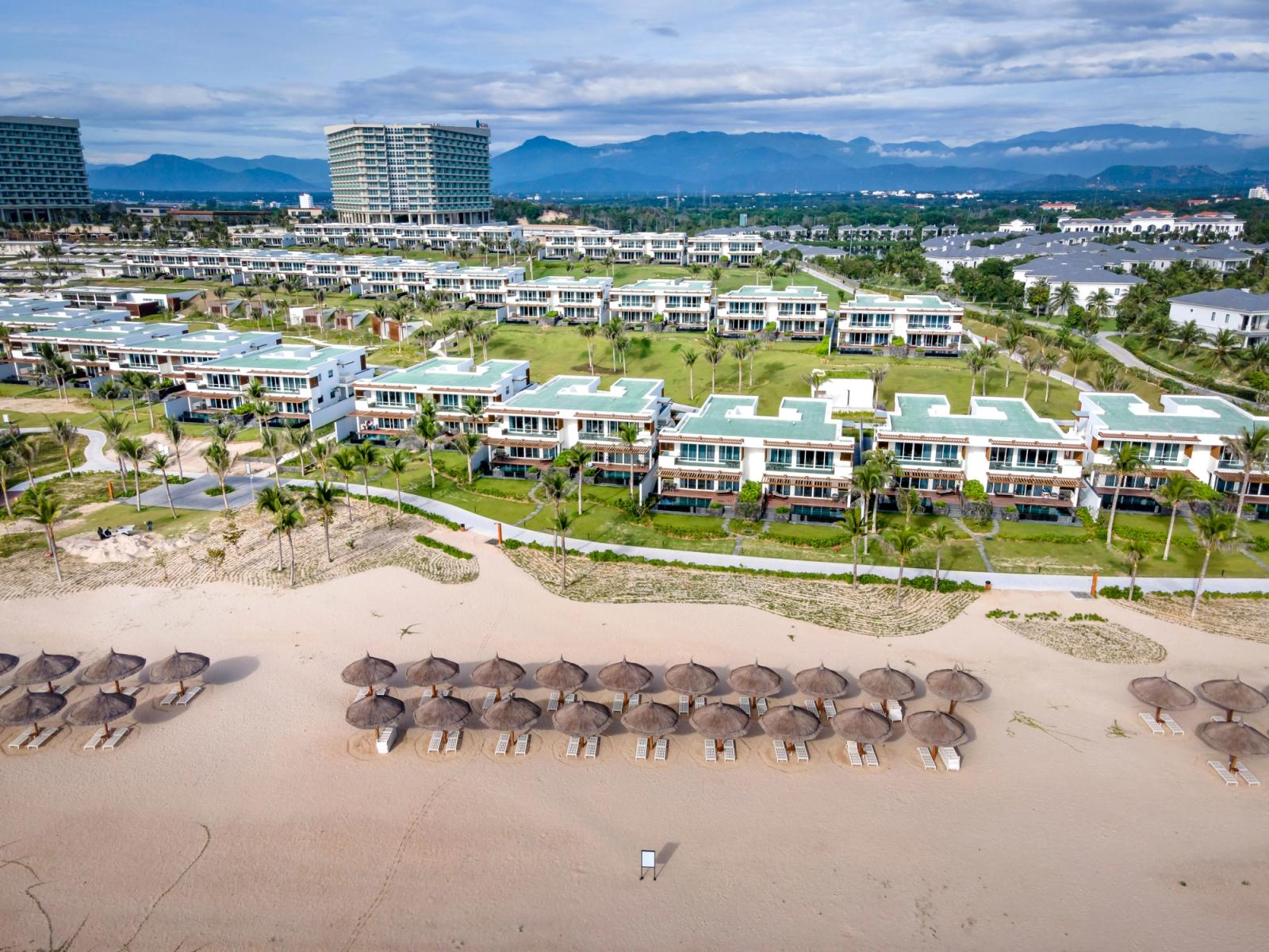 Aerial view showcasing a sprawling luxury beachfront resort with villas and palm-lined shore in Vietnam