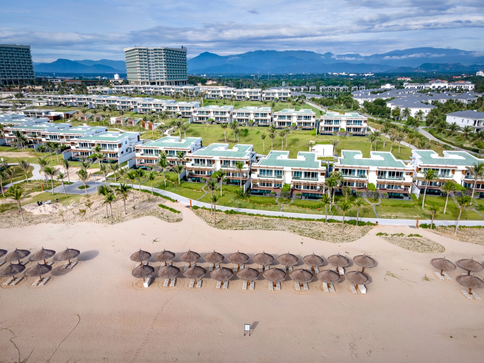 Aerial view showcasing a sprawling luxury beachfront resort with villas and palm-lined shore in Vietnam