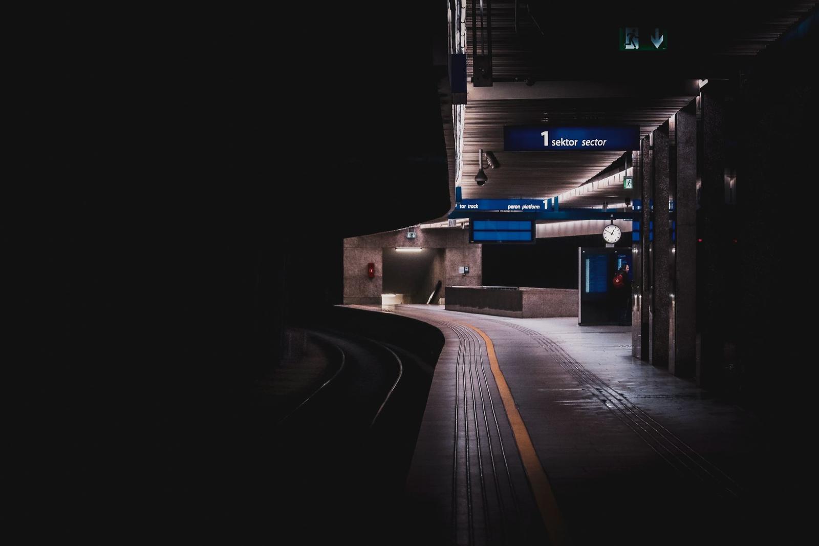 Dimly lit underground train platform with signage glowing along the tunnel