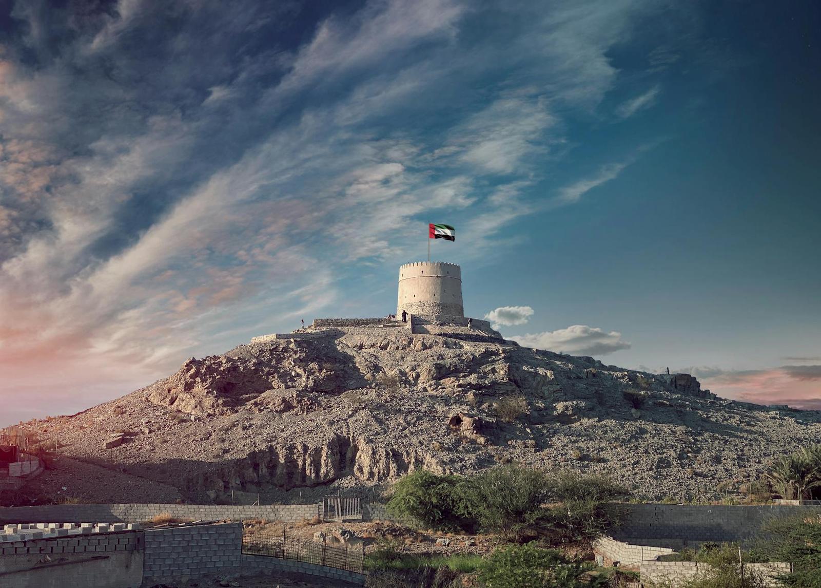 A stone watchtower on a rocky hilltop flying a flag at dusk