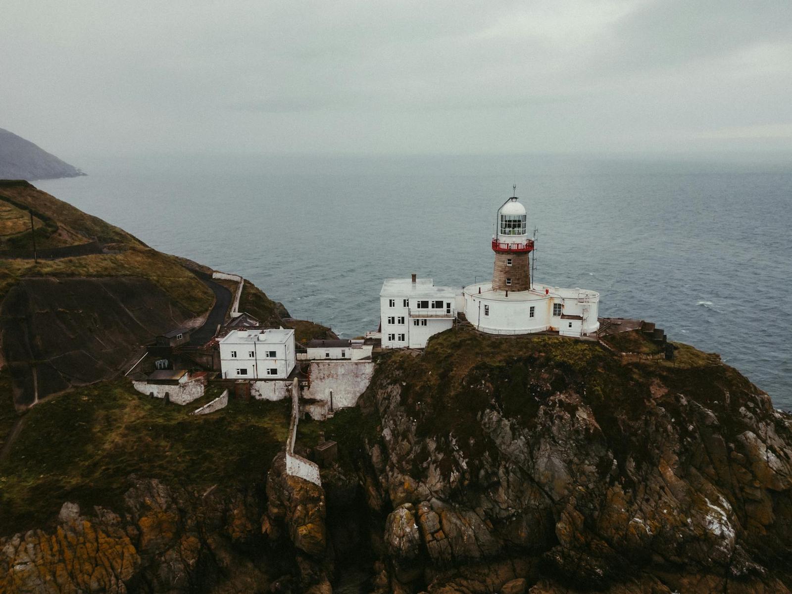 A white lighthouse perched on a rugged cliff above the sea