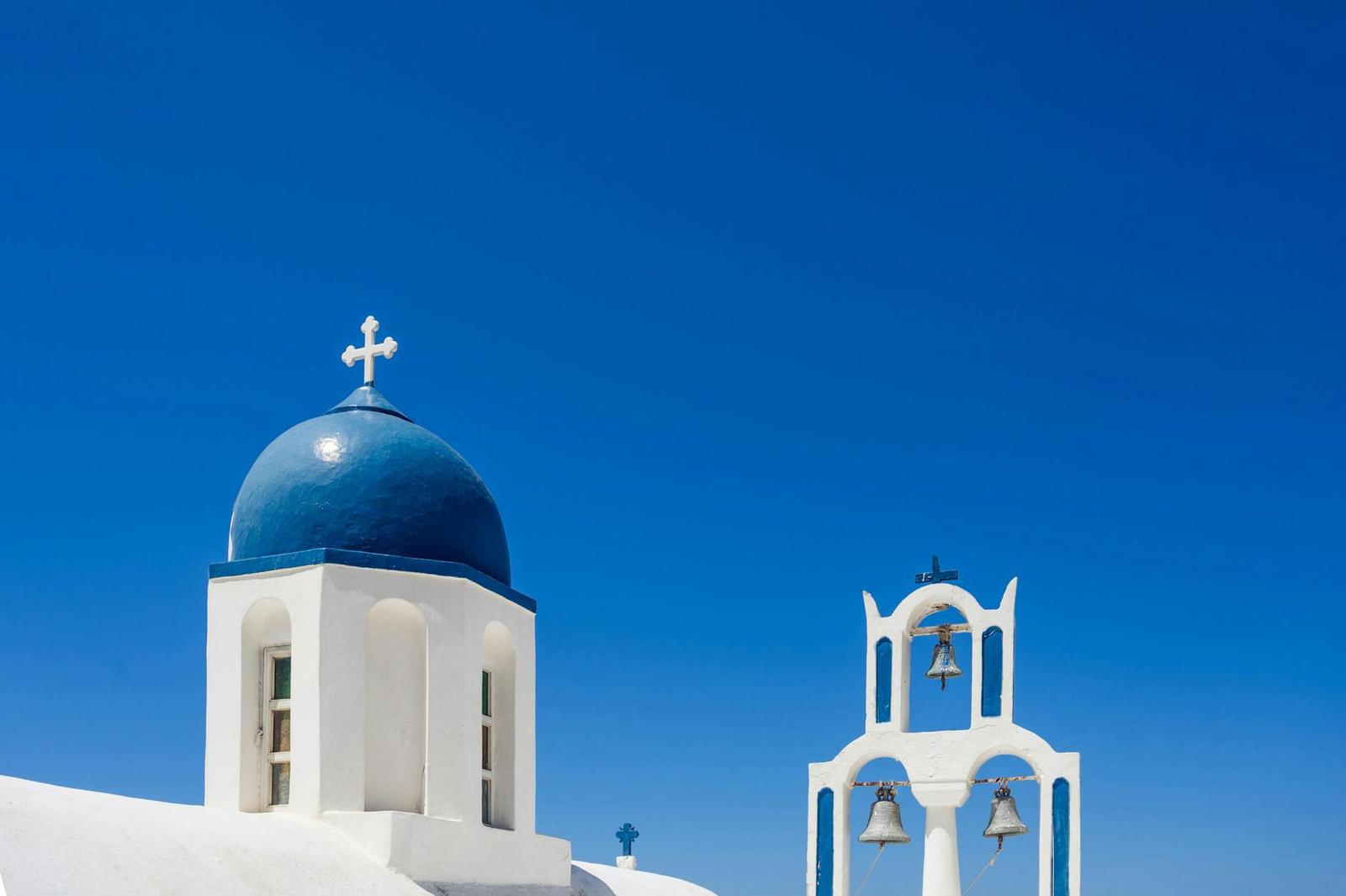 Iconic blue dome and bell tower of a church in Santorini under a clear blue sky