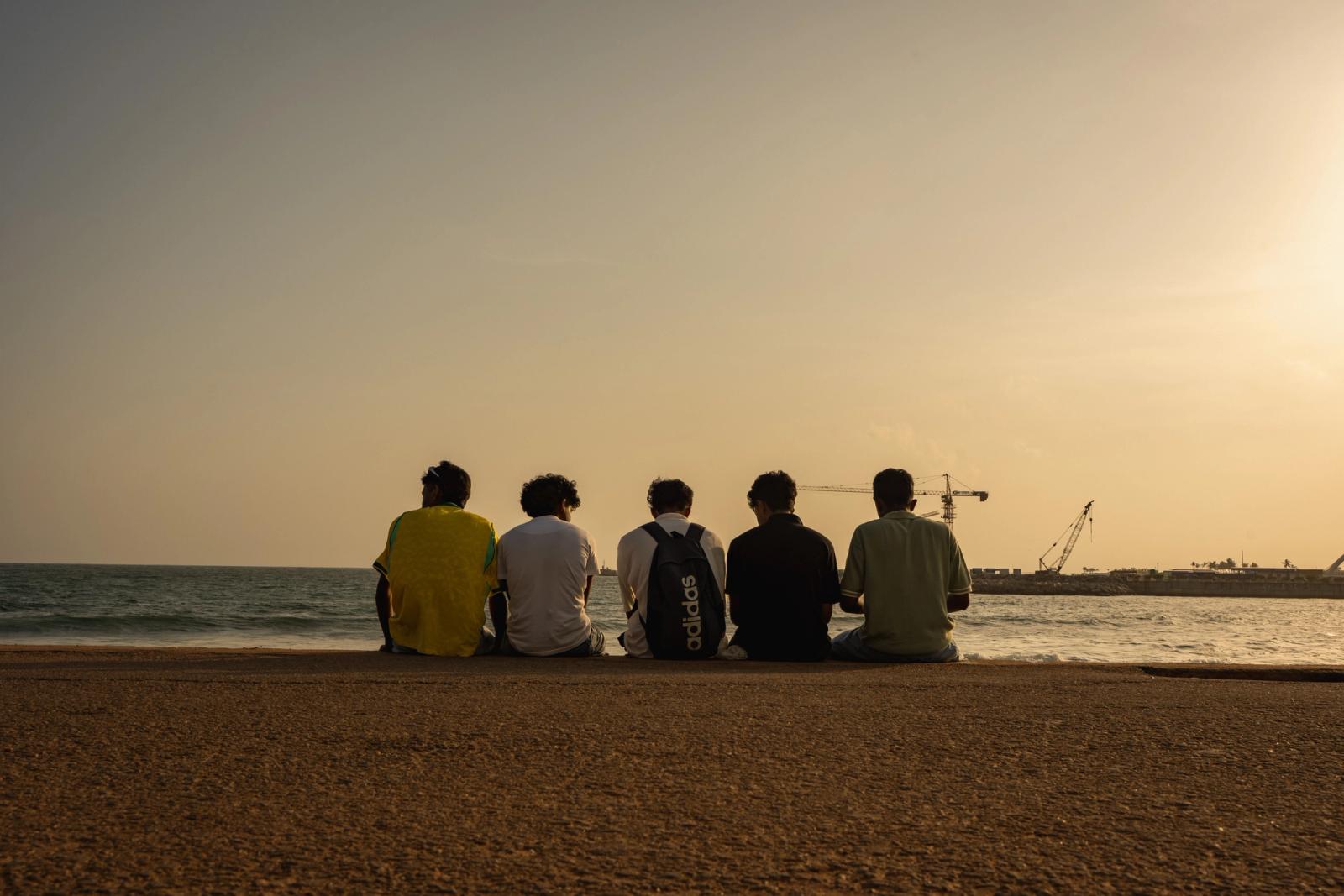 A group of teenagers sitting by the beach in Colombo, Sri Lanka, enjoying a serene sunset view