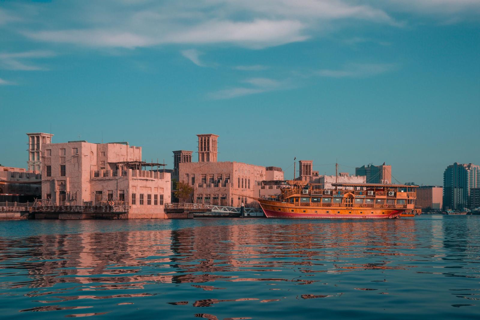 Scenic view of a traditional dhow boat near historical buildings along Dubai Creek at sunset