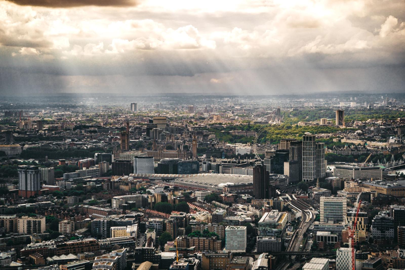 Aerial view of London's cityscape at sunset with dramatic cloud formations and sunbeams