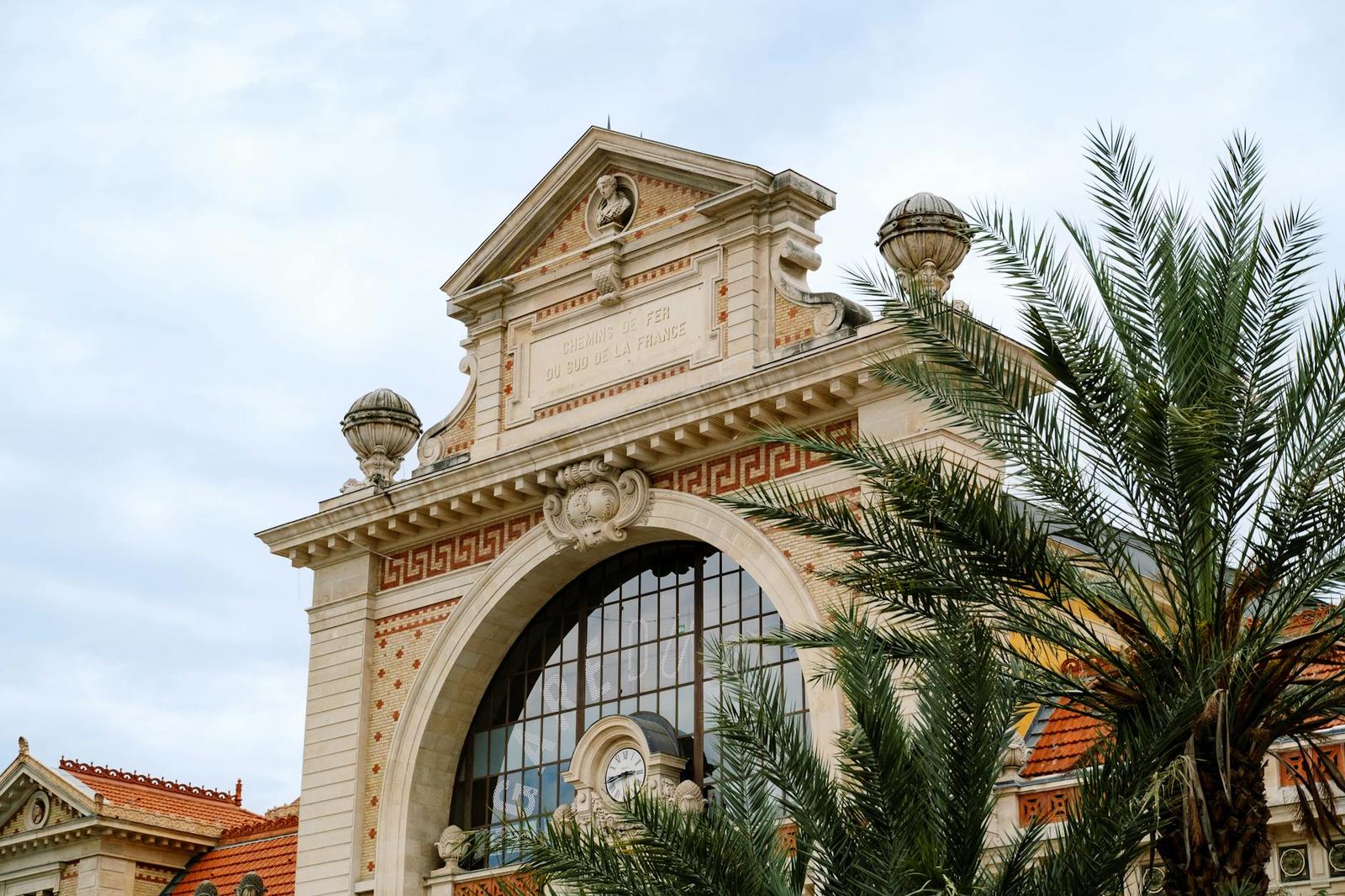 An ornate stone archway facade with a pediment behind a palm tree