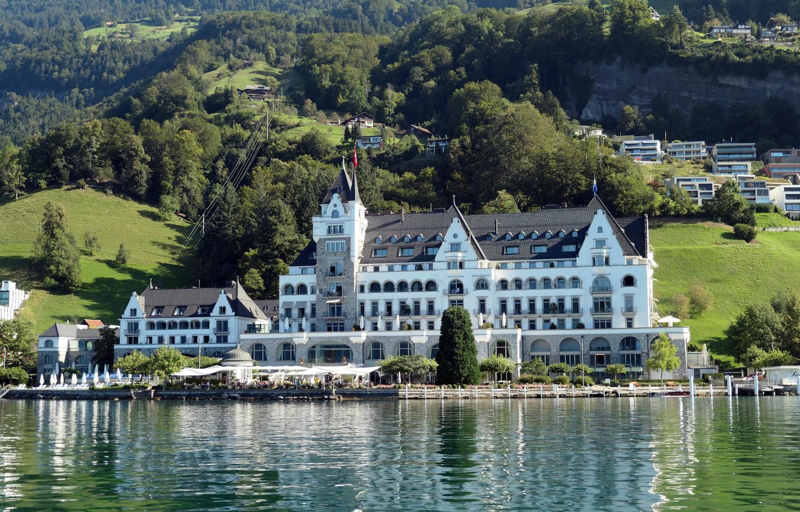 White castle-style hotel on a lakeshore backed by green hills