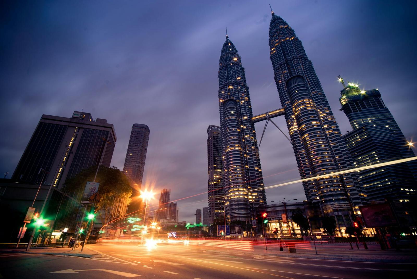 Twin skyscraper towers lit up above a busy city street at dusk