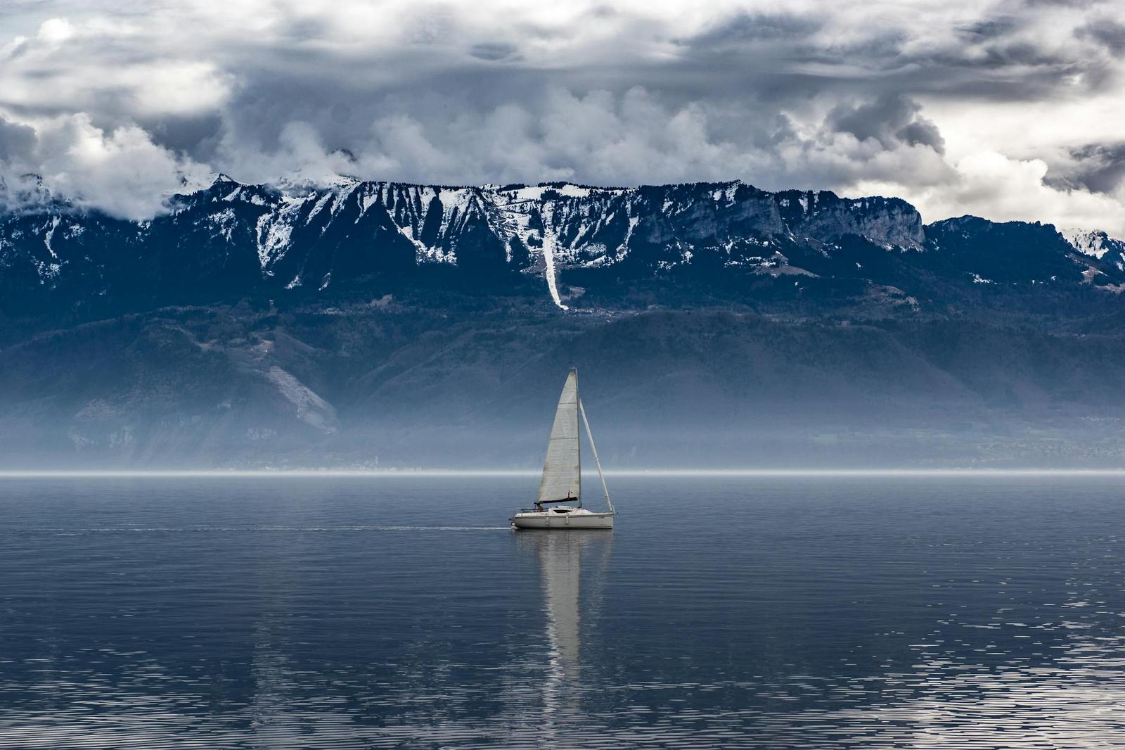 Sailboat crossing a calm lake beneath snow-dusted mountain ridges