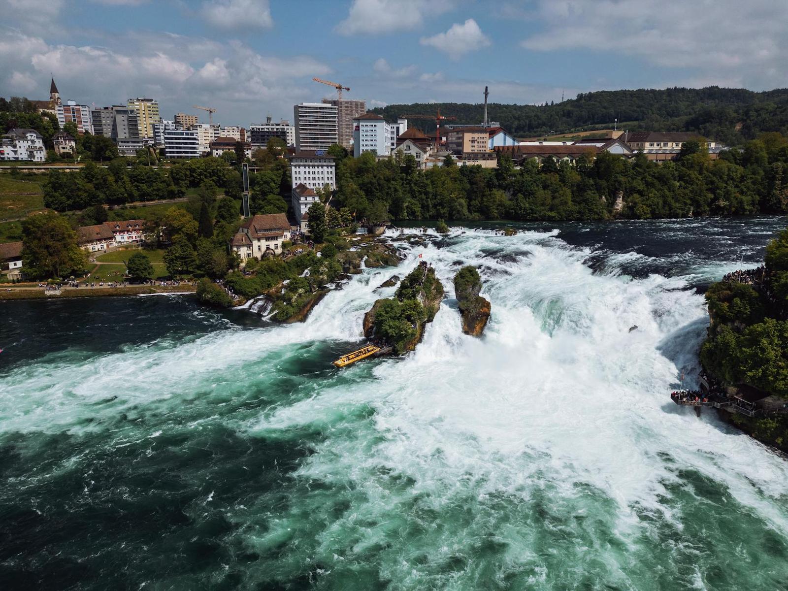 Wide waterfall cascading around rocky outcrops beside a riverside town