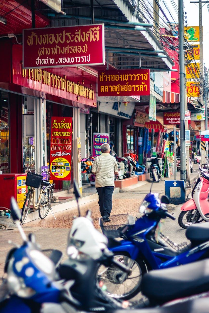 Man walking past parked scooters below red shop signage