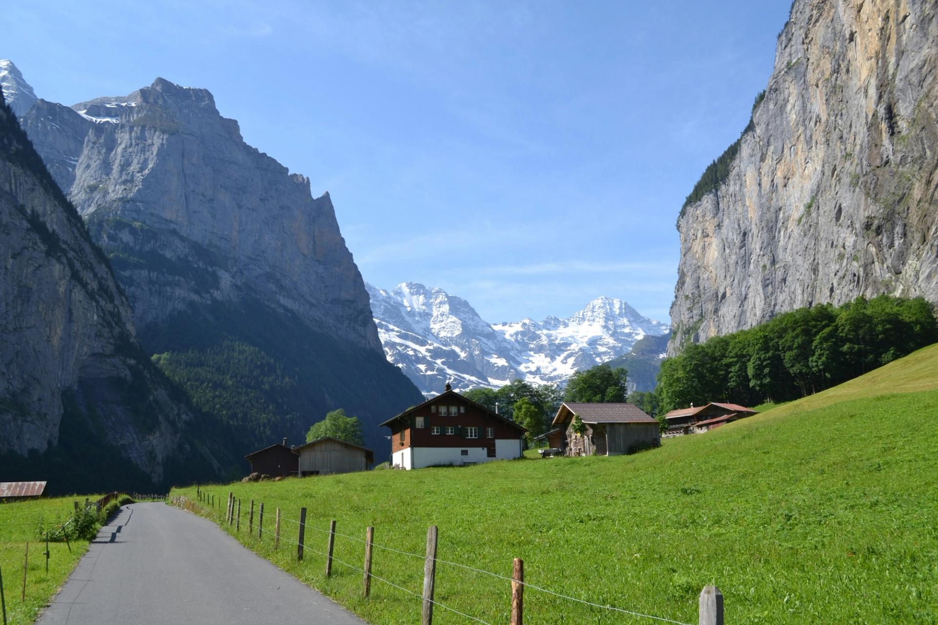 Wooden chalets in an alpine meadow flanked by sheer cliffs and snow-capped peaks