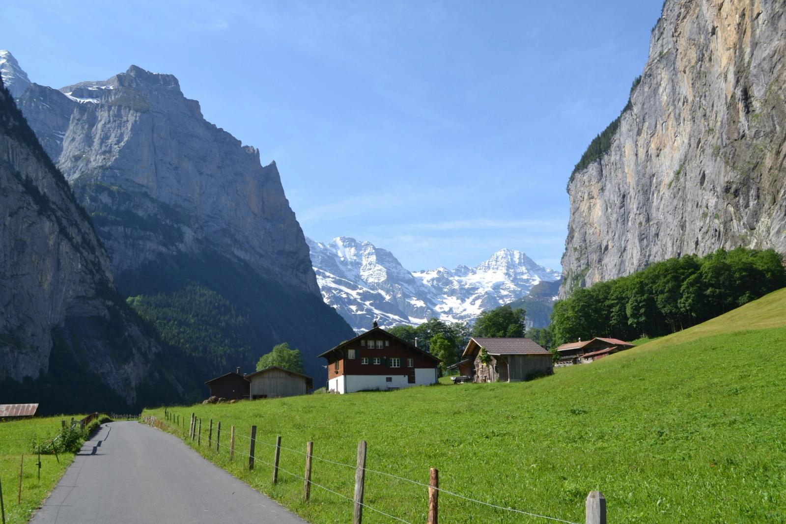 Wooden chalets in an alpine meadow flanked by sheer cliffs and snow-capped peaks