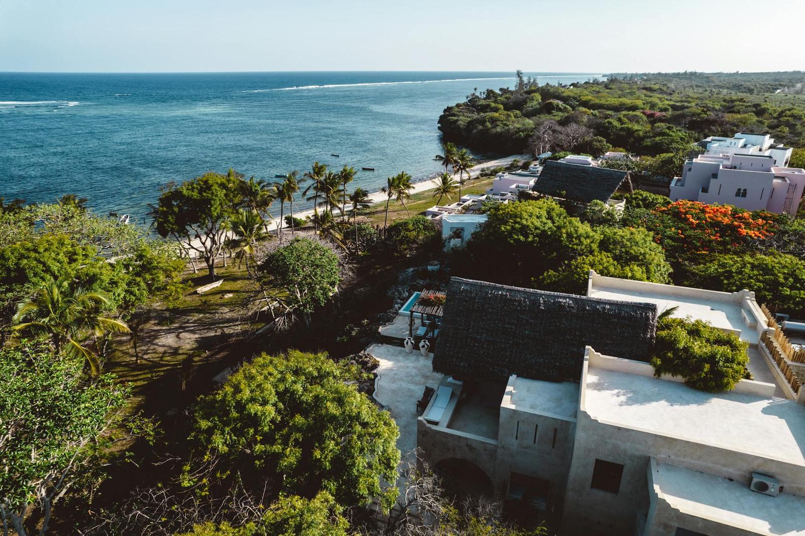 An aerial view of a whitewashed coastal villa above turquoise ocean and palms
