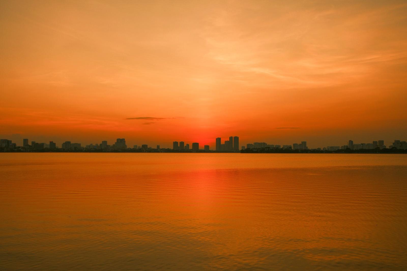A vivid sunset casts a golden hue over the serene waters of Hanoi, Vietnam
