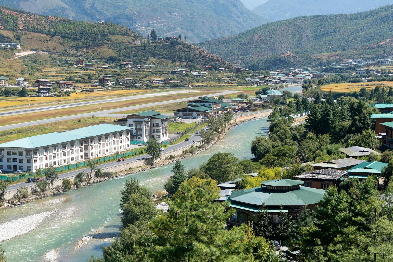 A riverside resort with green roofs beside an airstrip in a mountain valley