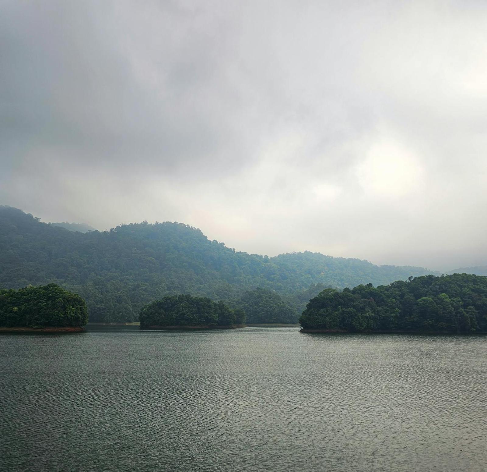 Serene view of Periyar Lake in Kerala, India with misty hills and dense greenery under cloudy skies