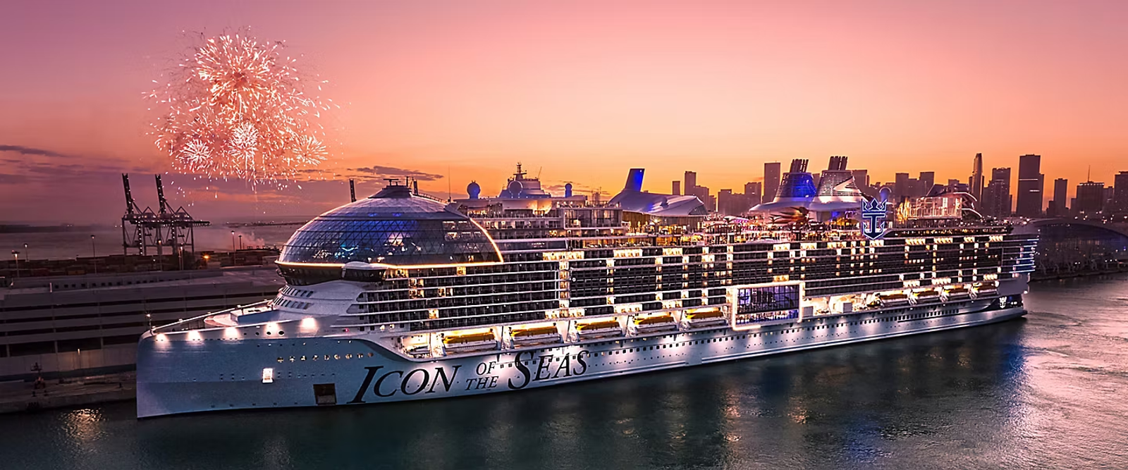 A brightly lit cruise ship docked at sunset with fireworks over the city skyline