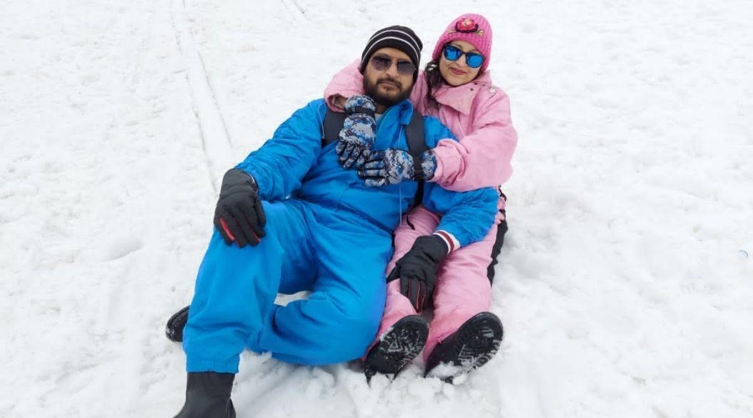 Couple sitting on snow in a winter landscape with mountains.