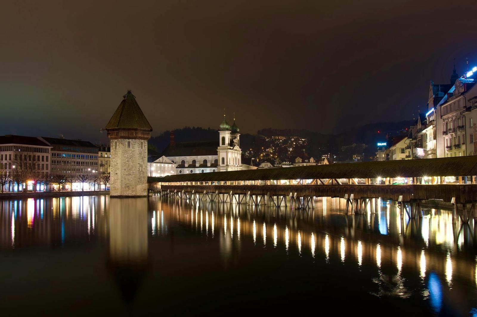 A wooden watchtower and covered footbridge over a river lit up at night