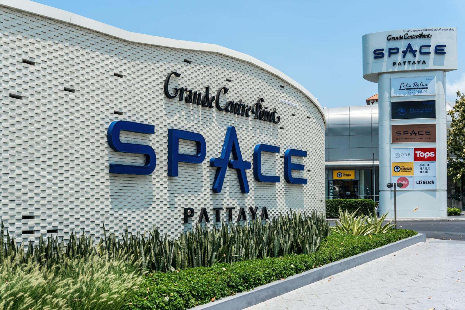 A modern shopping mall exterior with illuminated signage and landscaped entrance