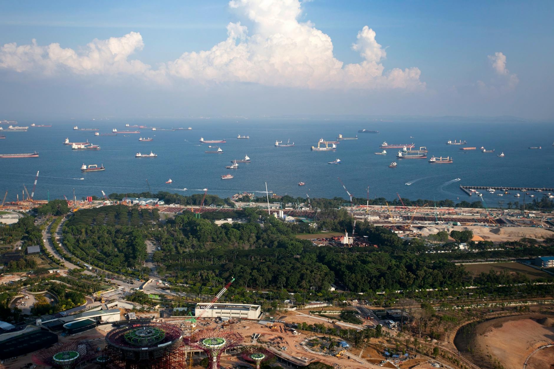 Aerial view of cargo ships anchored offshore beyond a green harbourfront park
