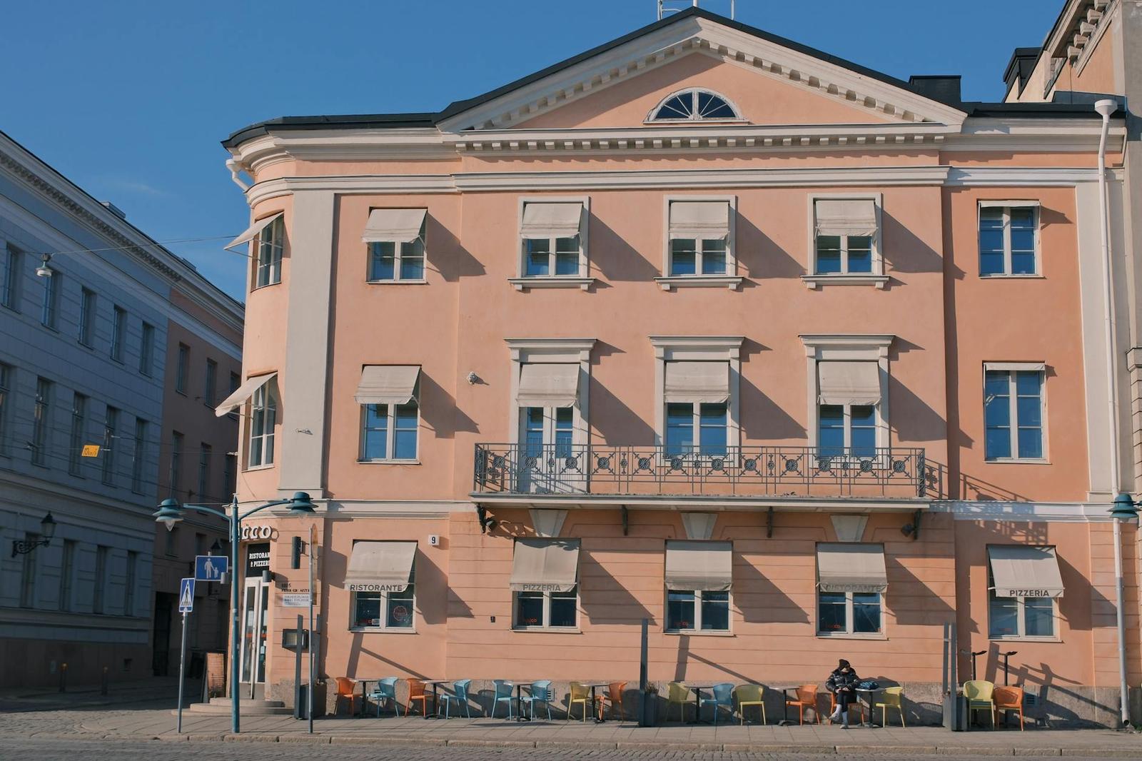 Pastel pink neoclassical facade with shuttered windows on a corner street