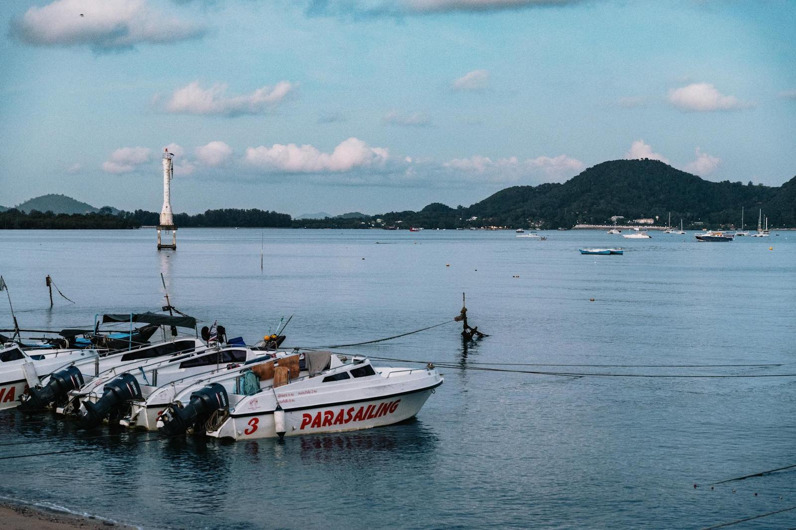 Speedboats moored along a harbor with hills and a lighthouse marker in the distance
