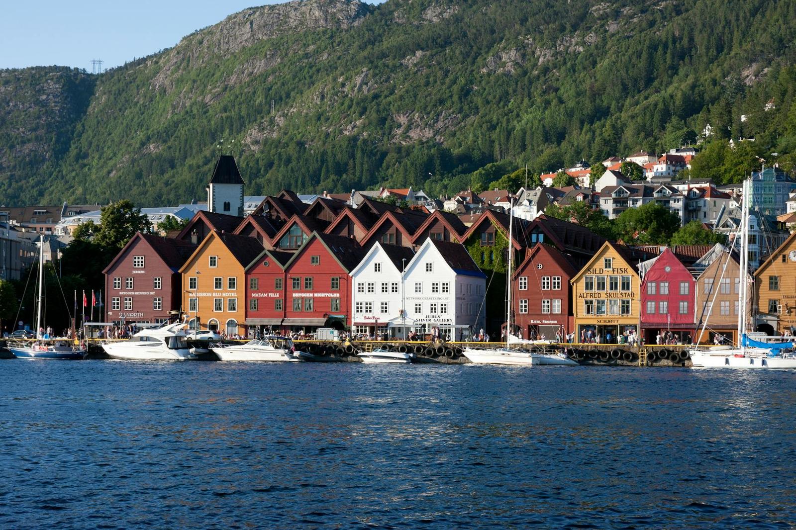 Rows of colourful wooden gabled houses along a harbour backed by a forested hillside