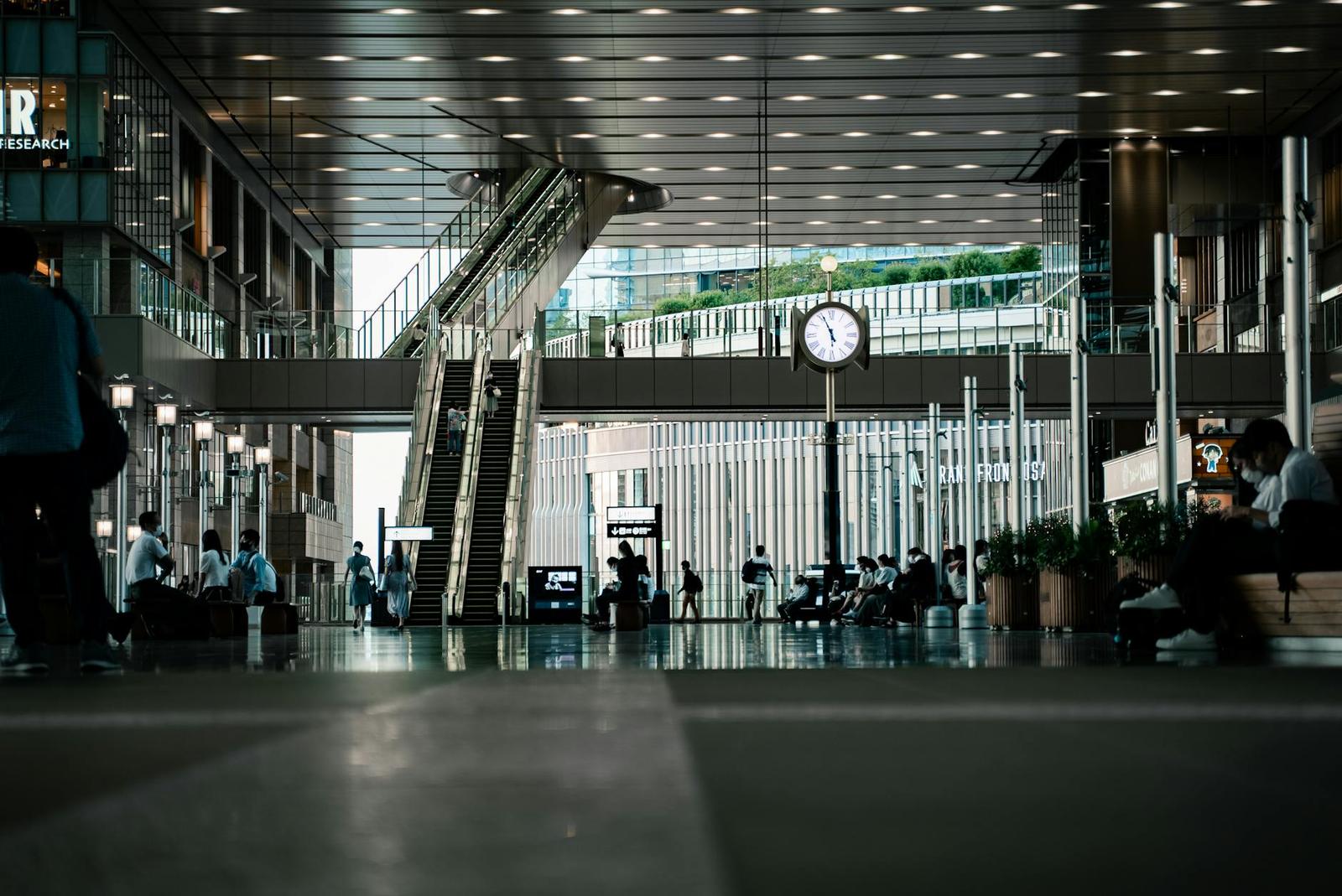 Travellers waiting in a modern station concourse beneath an escalator and clock
