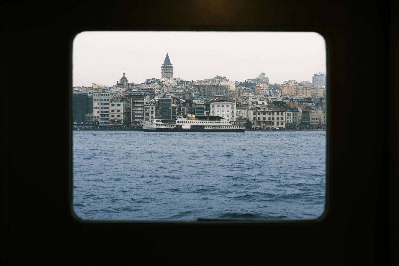 View through a ferry window of a hillside city and a passing boat
