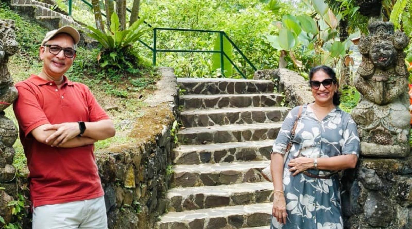 Couple posing at 'My Swing Bali' amid lush greenery and statues.