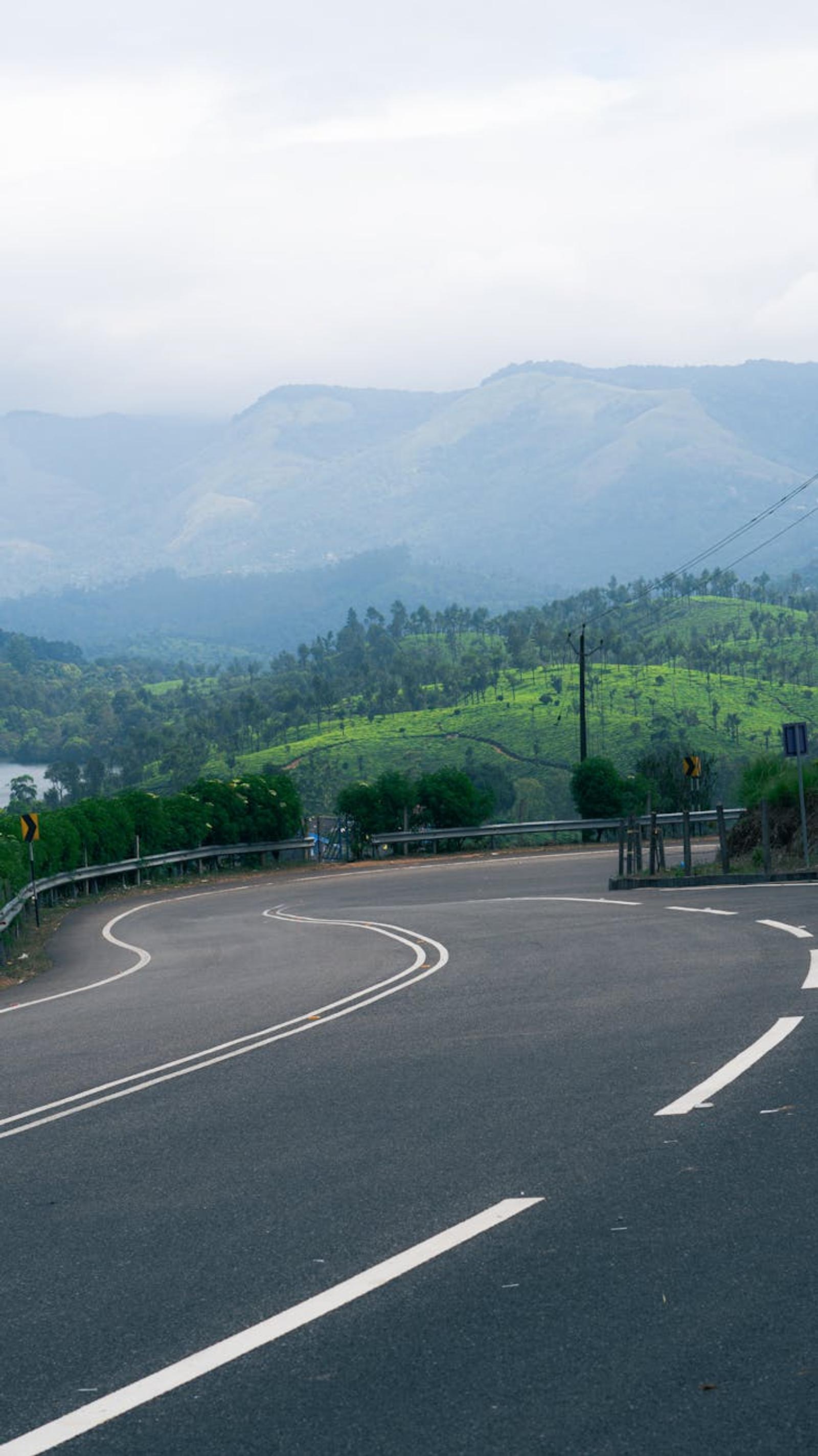 Winding road through lush greenery with distant mountains in Kerala, India