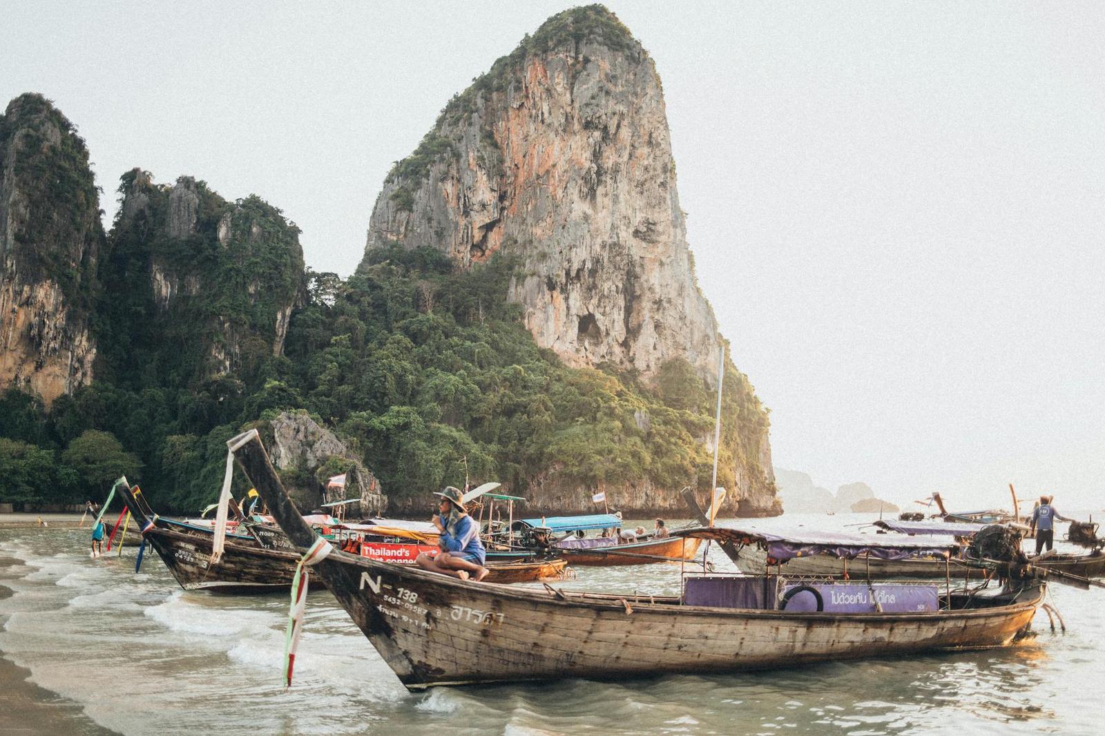 Longtail boats beached below a towering limestone rock formation at golden hour