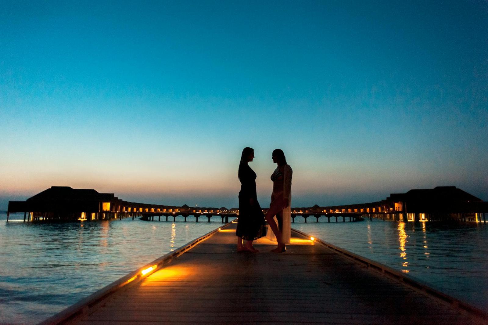 Two women silhouetted on an overwater walkway at dusk