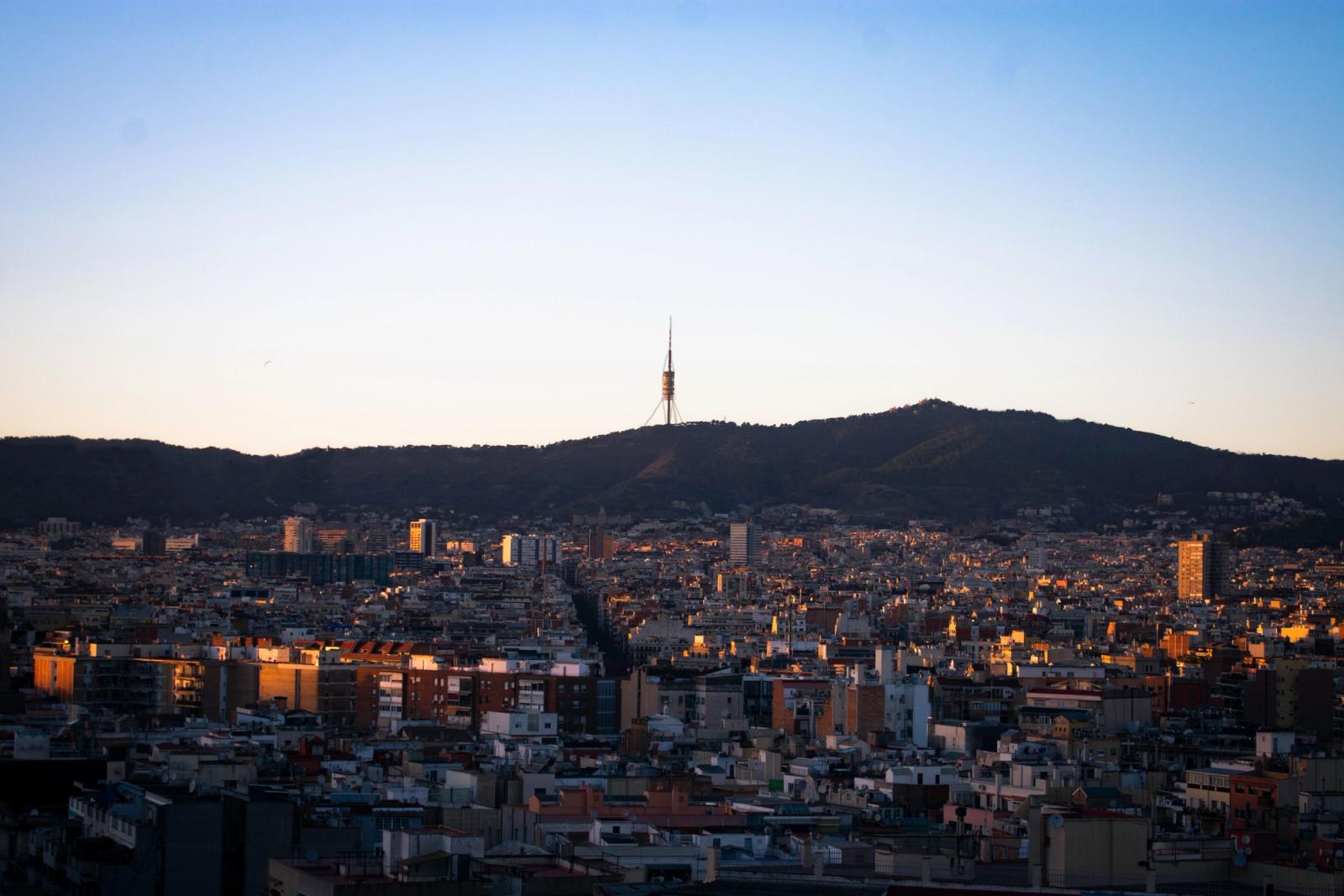 A cityscape of Barcelona with the iconic Collserola Tower against a dawn sky