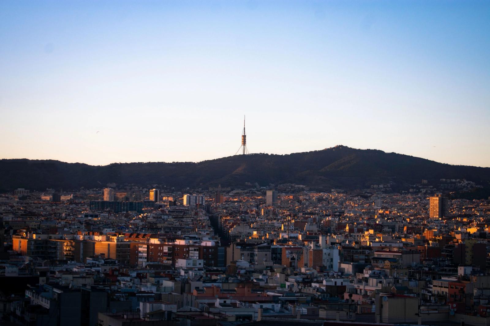 A cityscape of Barcelona with the iconic Collserola Tower against a dawn sky
