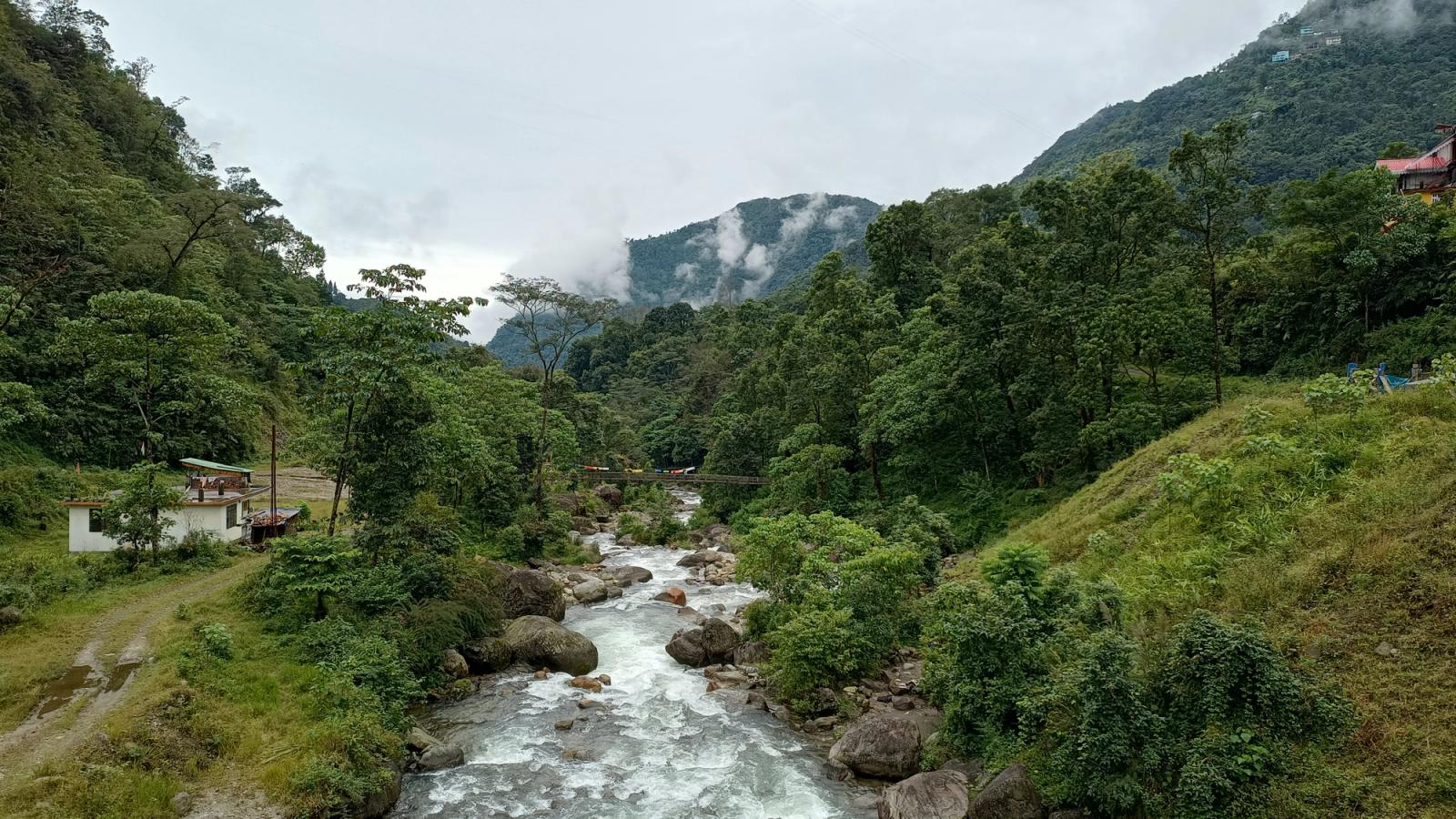 A peaceful river flowing through misty mountains and dense forests in Sikkim, India