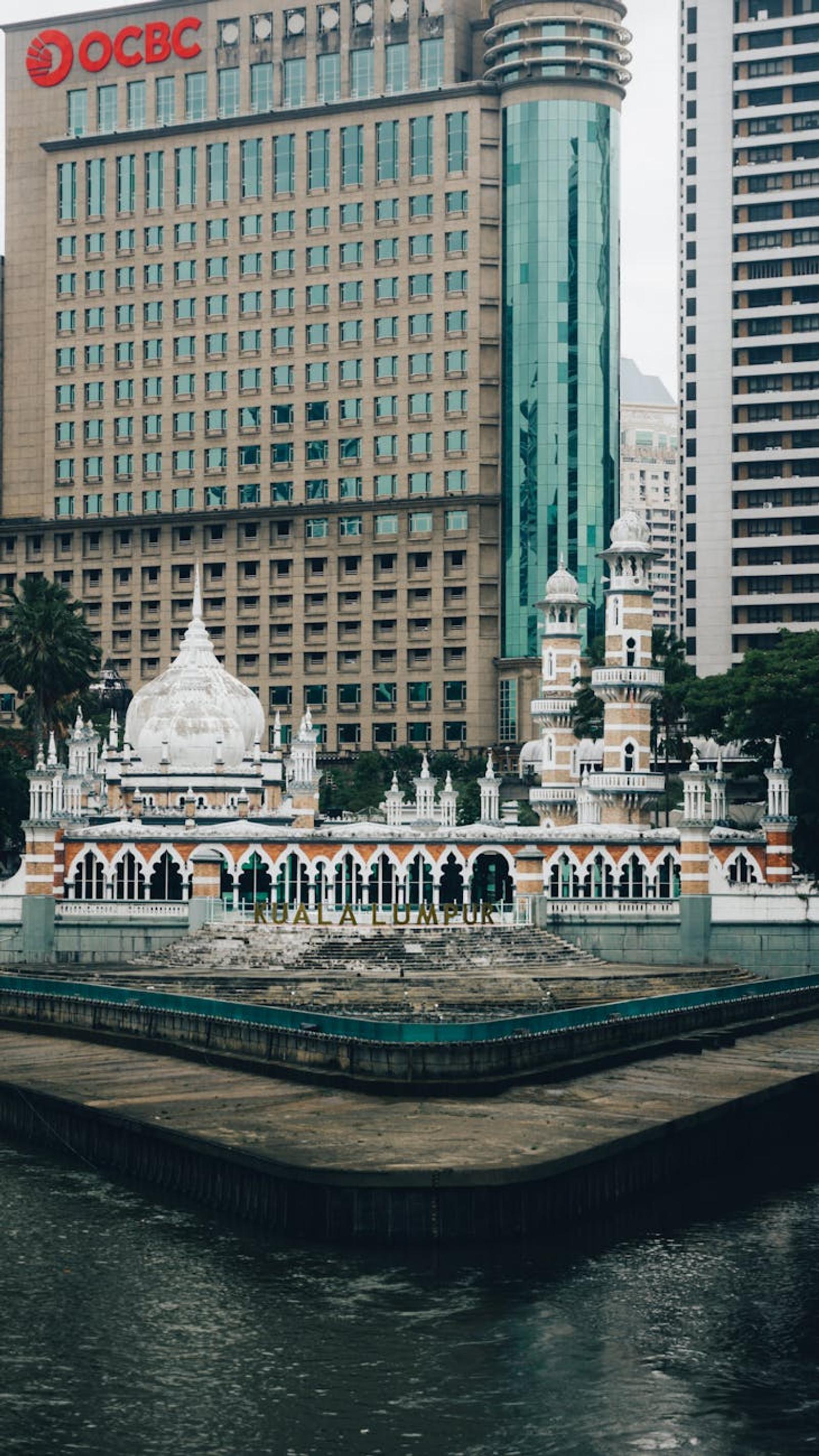 Domed mosque and minarets at a river confluence framed by high-rise towers