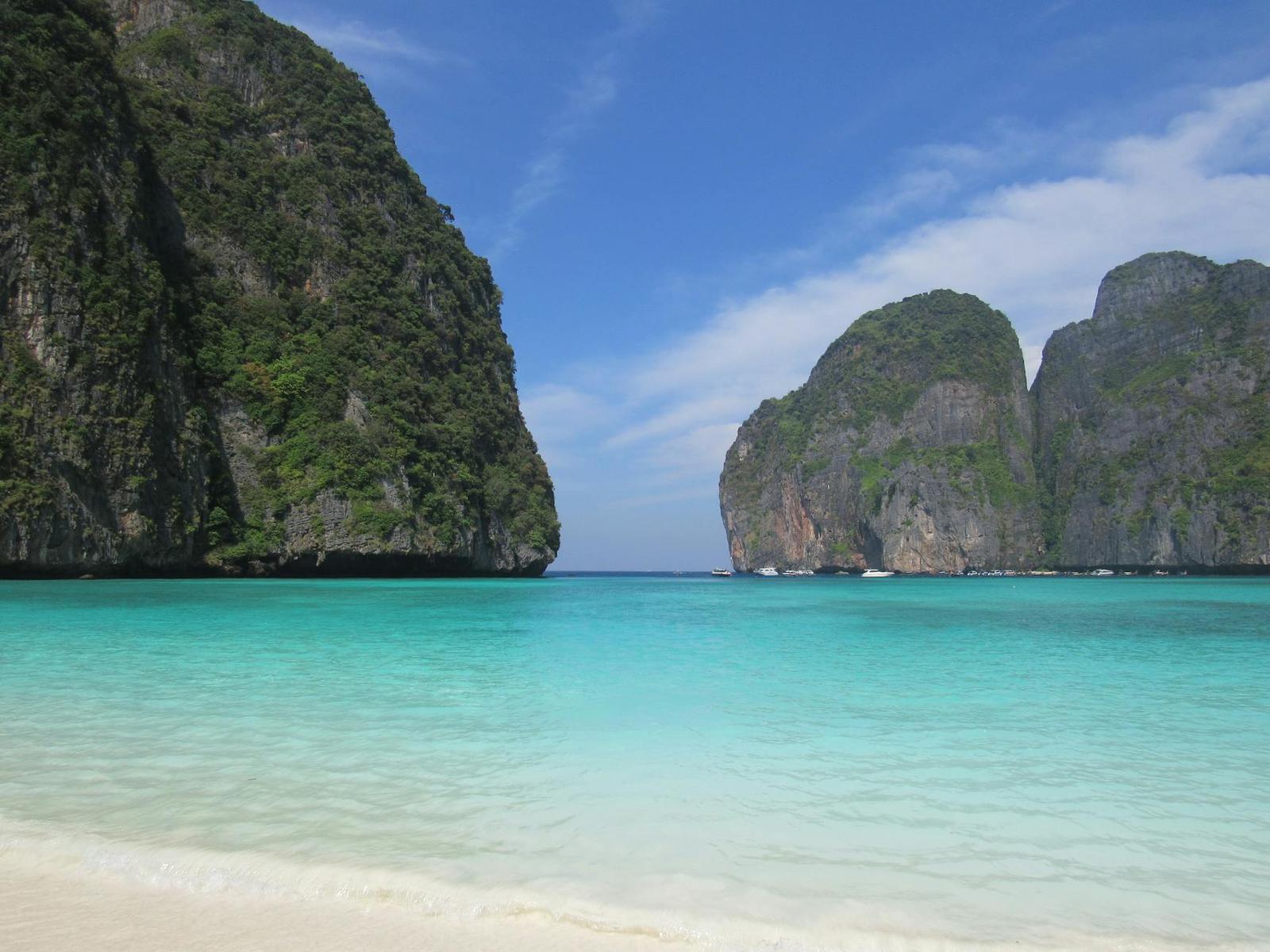 White sand beach beside turquoise water framed by jungle-covered limestone cliffs