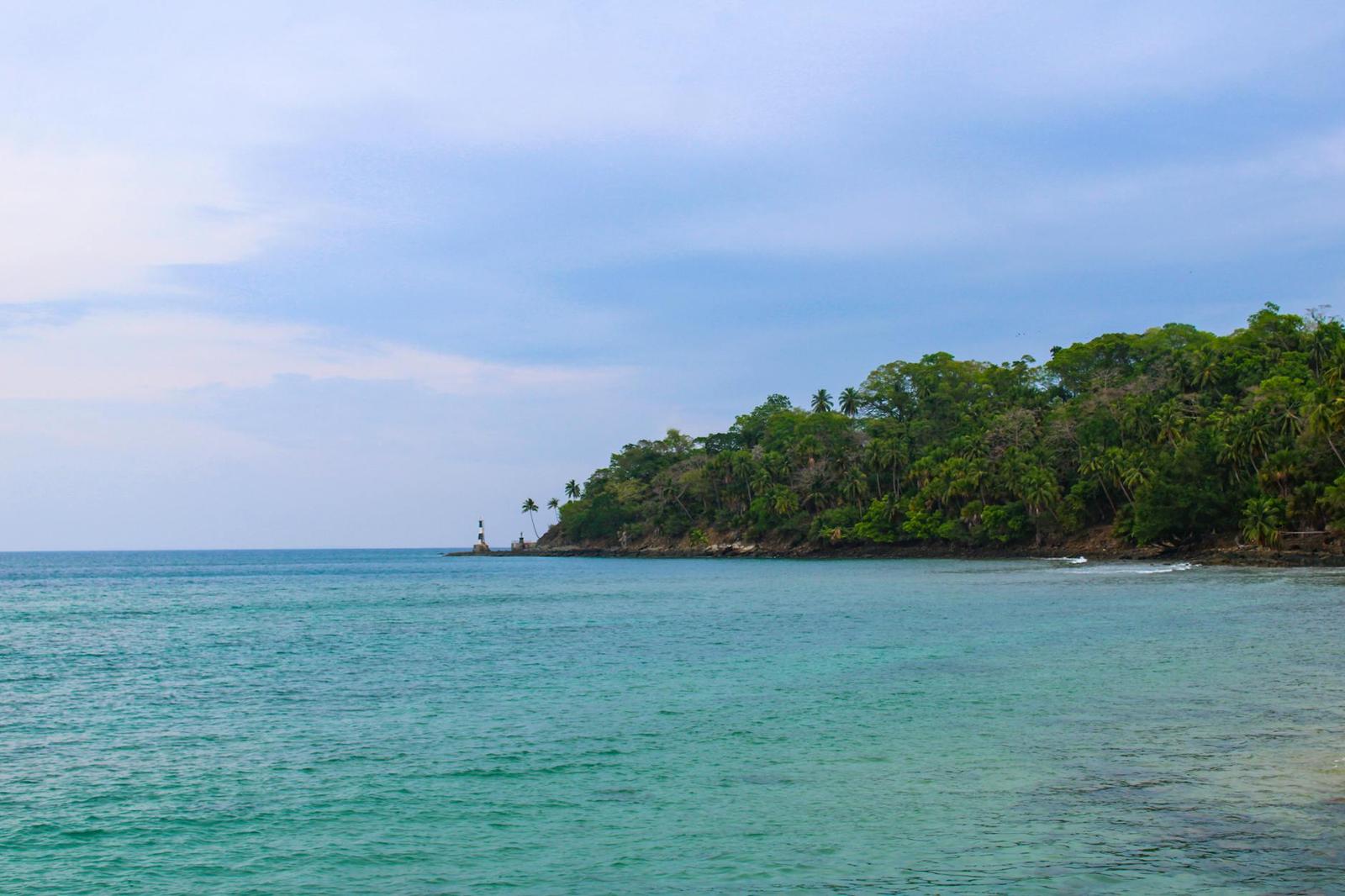 A wooded headland with a small lighthouse meeting calm turquoise water
