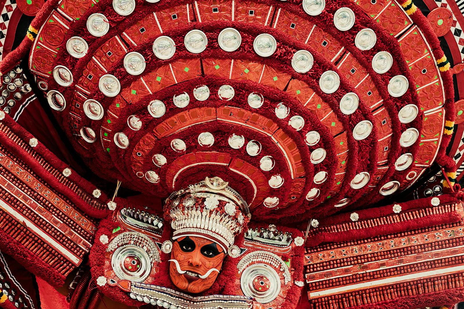 Close-up of an elaborate red ceremonial headdress framing a painted face