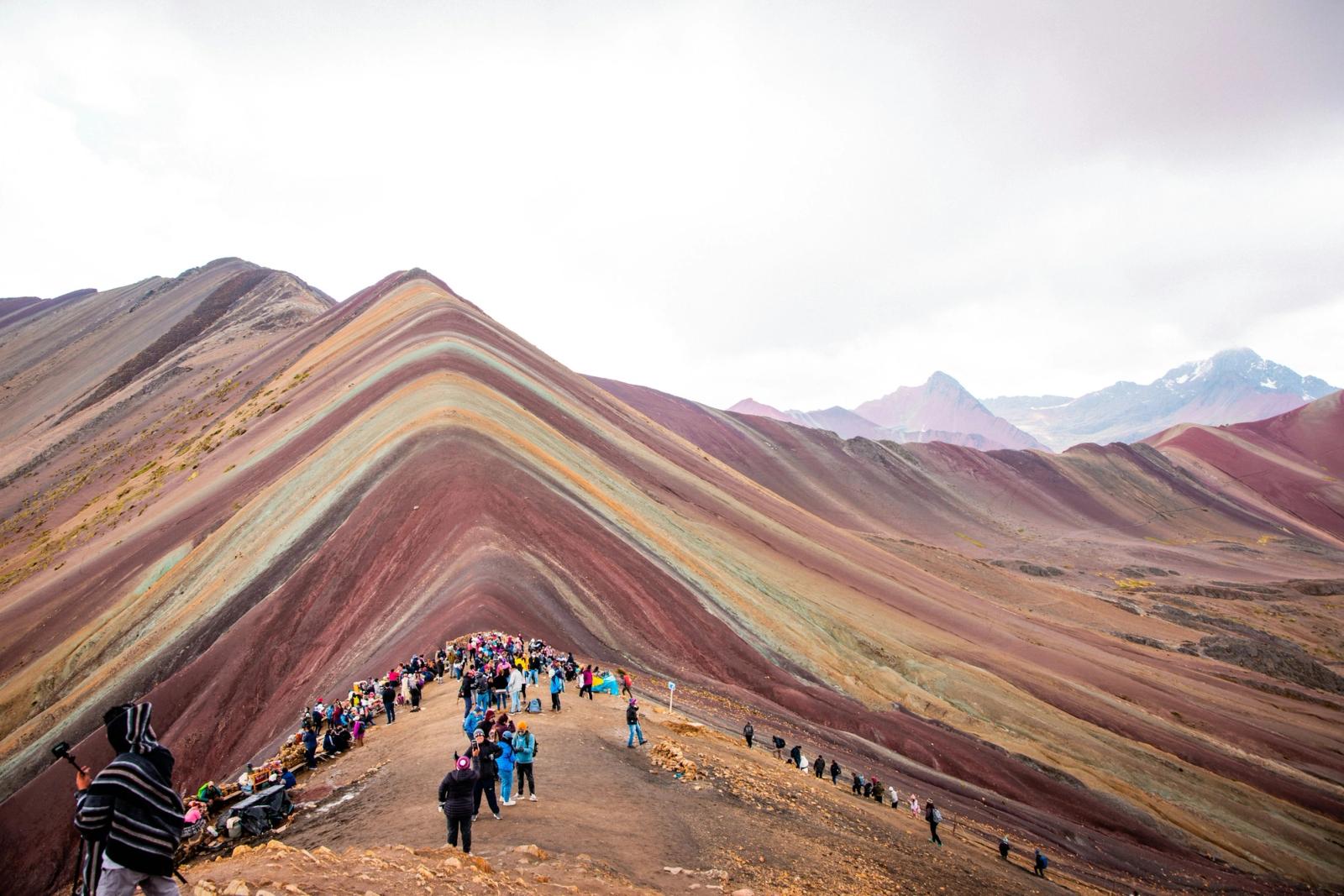 Hikers climbing a striped multicoloured mountain ridge