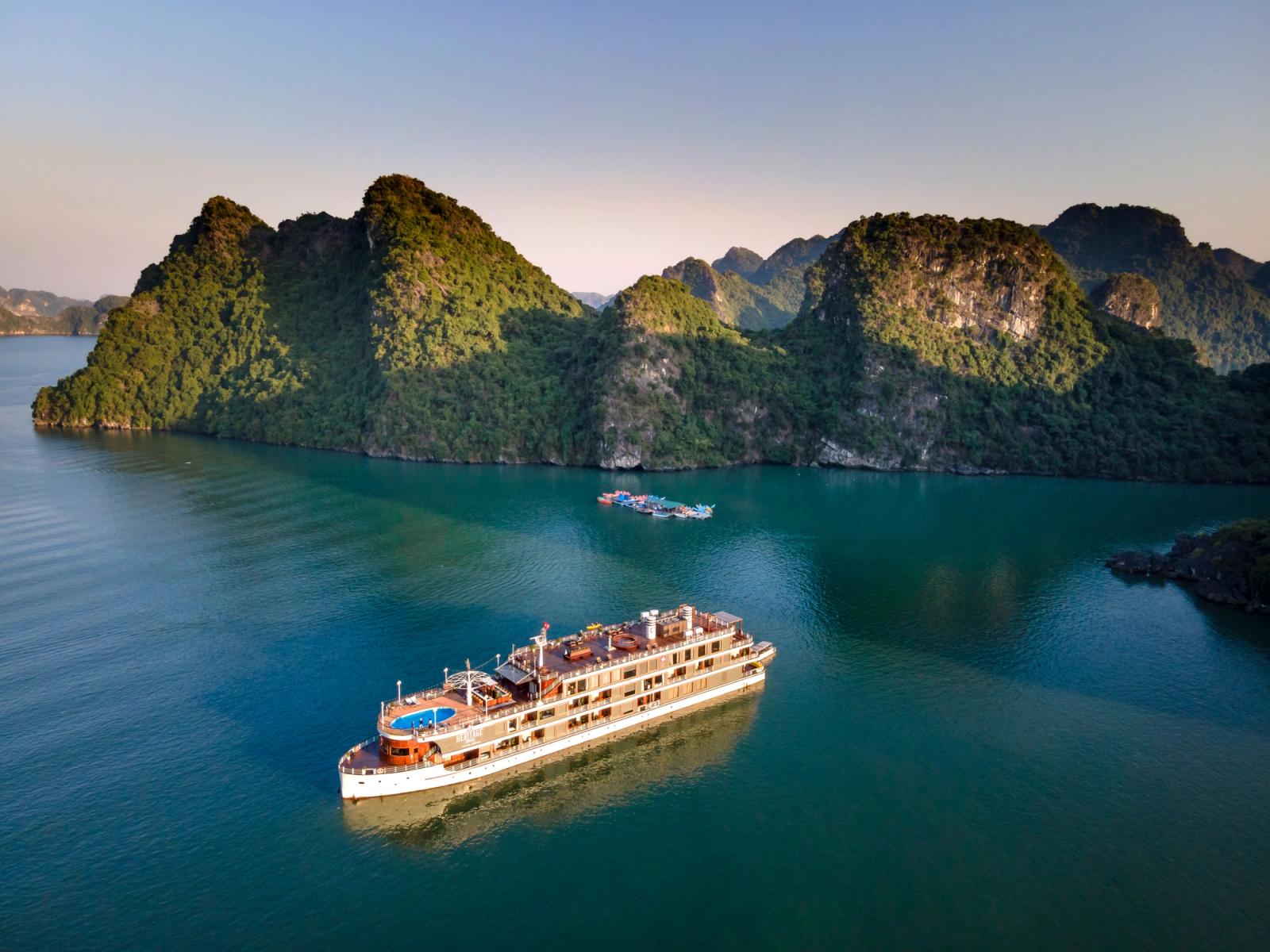 A cruise ship navigates the tranquil waters of Halong Bay with stunning limestone cliffs in the background