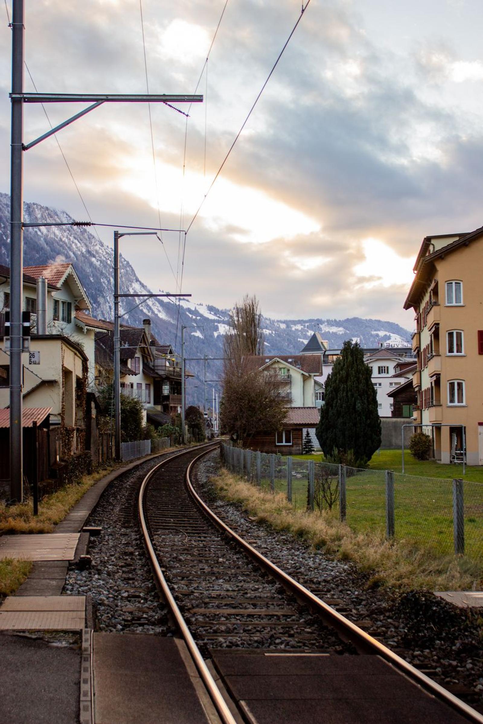Railway curving past chalets toward snow-capped hills at dusk