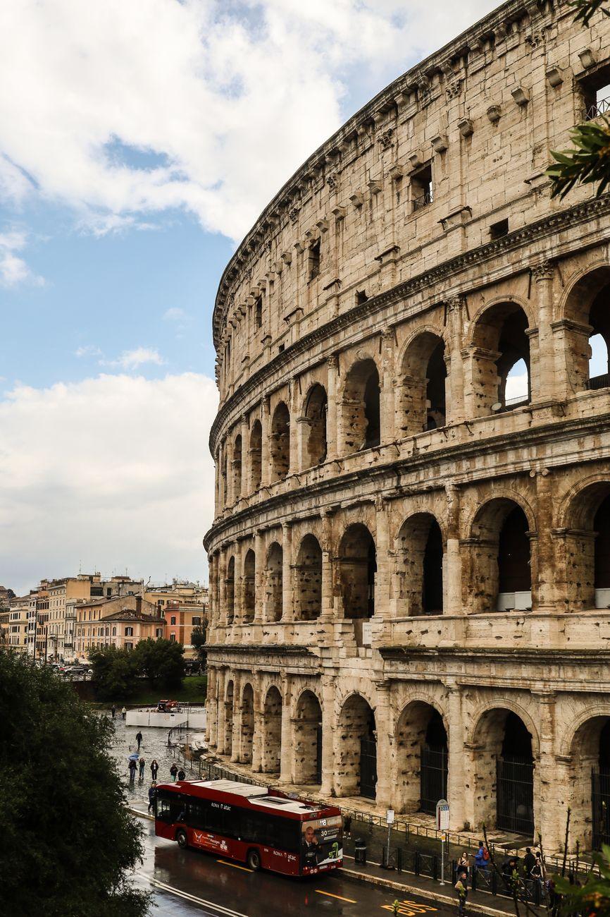 Multi-tiered ancient stone amphitheatre with a sightseeing bus passing below