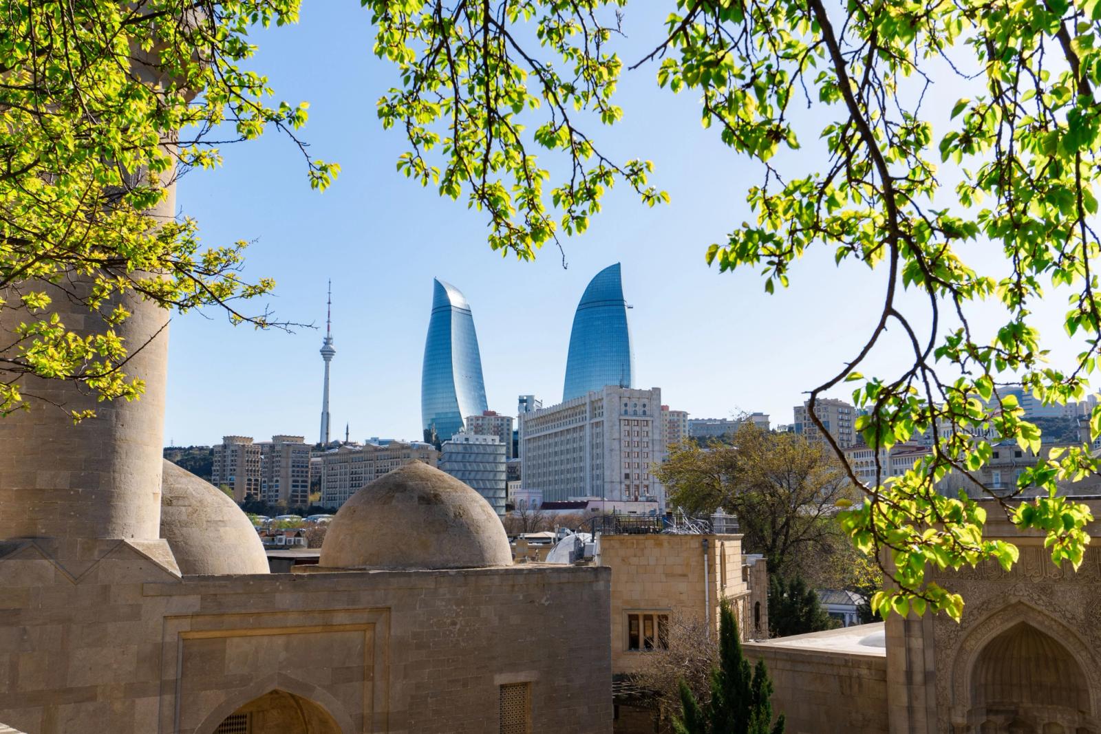 Vibrant spring view of Baku's Flame Towers framed by lush green leaves and historic architecture