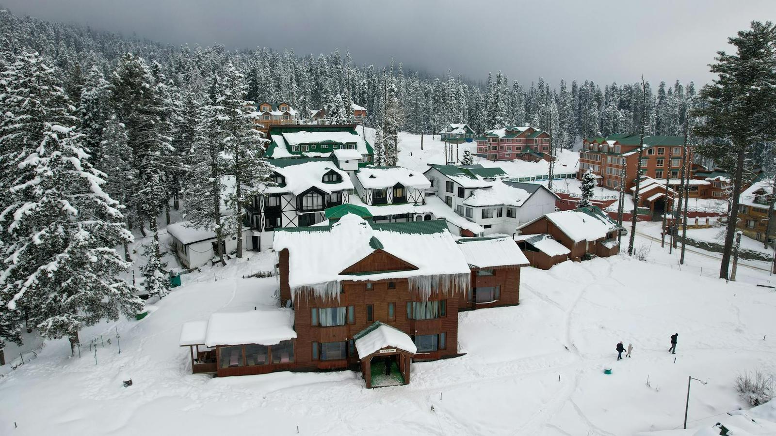 Aerial view of a snow-covered timber lodge complex with people walking outside